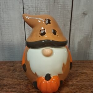 A ceramic gonk (a Scandinavian-style gnome) in rich autumnal tones like orange and brown, often with cut-out leaf or heart details in the hat that cast a soft, flickering glow when lit