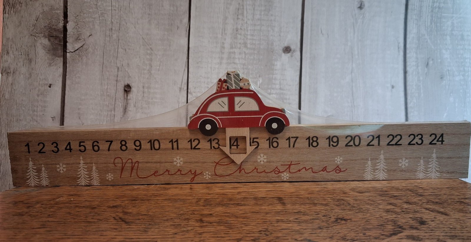 Car Wooden Advent Calendar 1 An advent calendar that is a length of wood that is 40cm and has a red car on top with an arrow with a window that slides from left to right marking the days til Christmas