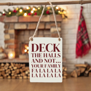 The card hangs elegantly in front of a softly lit, rustic fireplace adorned with twinkling fairy lights and sprigs of holly, casting a welcoming glow over the scene. The warm, neutral tones of the stone hearth and a draped tartan blanket in the background complement the sign’s festive message, infusing the composition with a cosy, joyful holiday ambience. Subtle bokeh lights add depth and a touch of seasonal magic without distracting from the card’s witty sentiment.